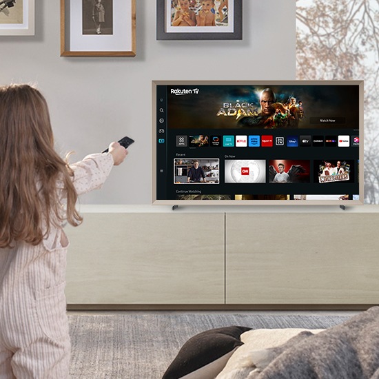 Một cô gái đang hướng điều khiển từ xa về phía The Frame, nơi hiển thị màn hình chính của Smart Hub.