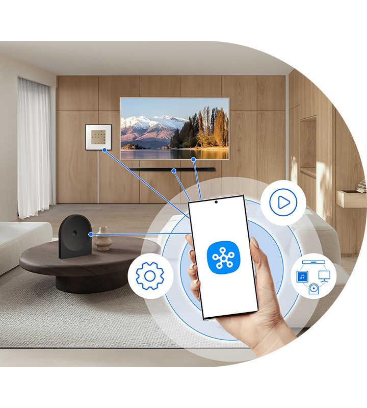 Hand holding a phone with the SmartThings app, wirelessly controlling compatible devices, including Music Studio 5 speaker.