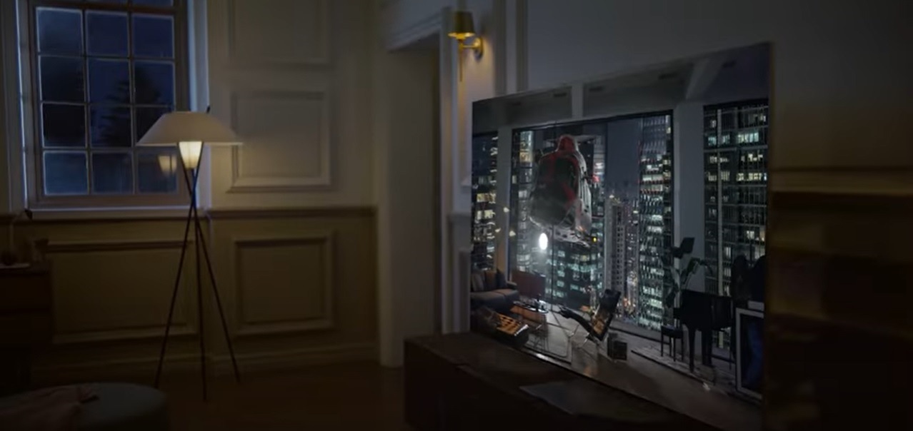 A Neo QLED TV is displaying a helicopter shooting light onto a building at night. Sound waves from its top channel speakers are filling the room.