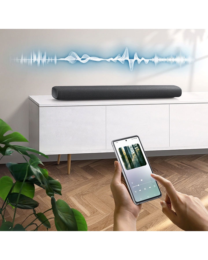 User plays music on their smartphone directly from their soundbar, which has soundwave graphics above it, using Music Mode which allows easy smartphone connectivity so optimized sound can be heard from soundbar.