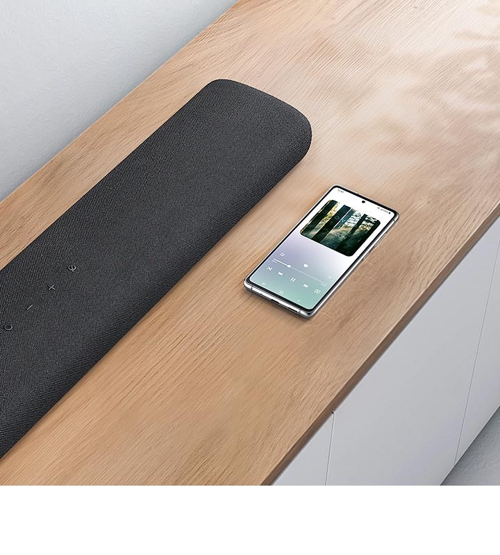 A smartphone which is showing music screen, sits next to Samsung S60A soundbar demonstrating Bluetooth connectivity for smartphone music playback.