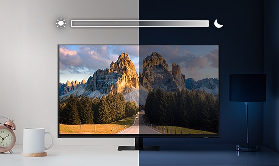 Samsung M7 Smart Monitor sits on top of a desk and is split into left and right sides. The left side is brightly lit while the right side is very dark. Above the screen is a slider icon with a sun on the left and a moon on the right.