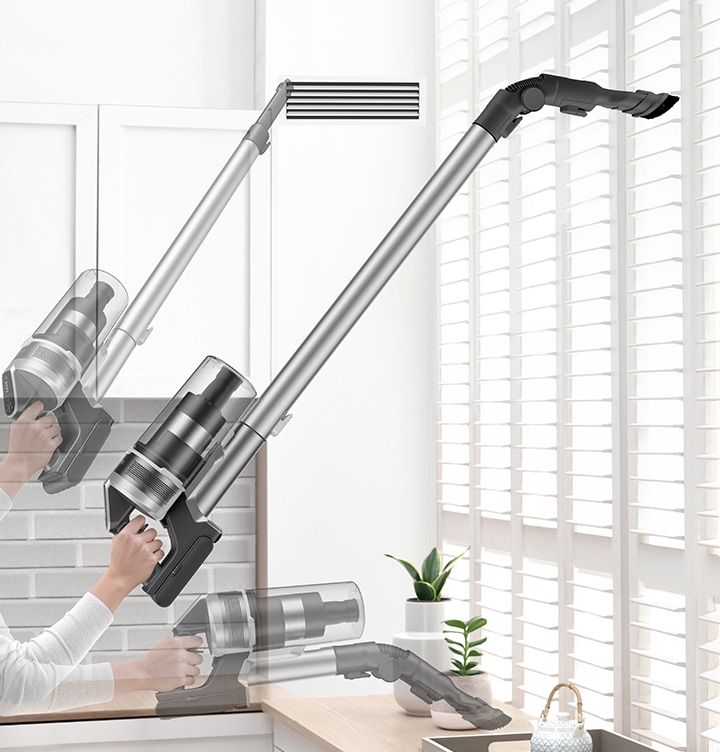A person lifts VS7500 with one hand and Cleans vent with the crevice tool and cleans blinds and table with the combination tool.