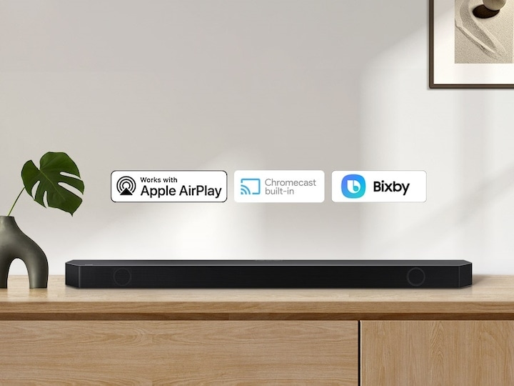 Alexa logo and Apple AirPlay logo can be seen along with Samsung Q990B soundbar which is sitting on living room cabinet.