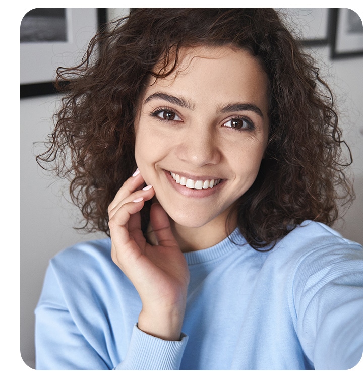 A woman taking a selfie. She's seen clearly but the background is blurred.