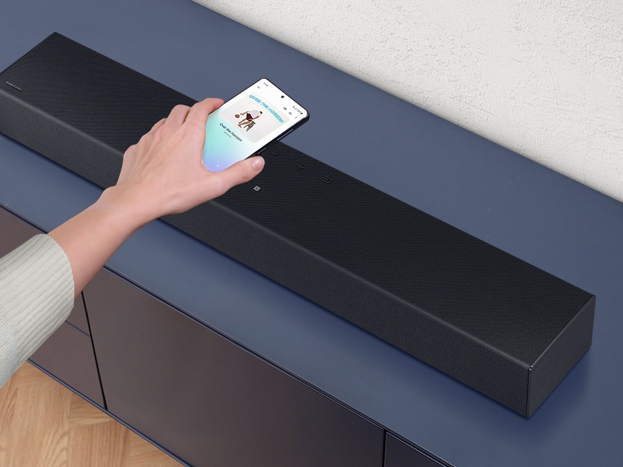 A hand places a smartphone with the Samsung music app on the Soundbar and easily mirrors their mobile audio.