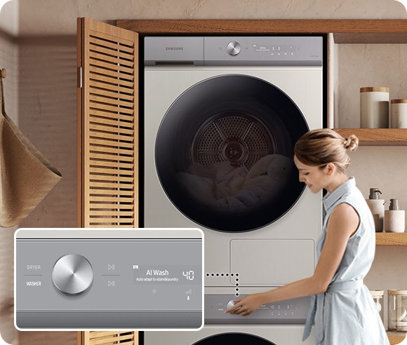 A white Bespoke Grande AI washer and dryer set is stacked vertically in a cabinet that has a wooden door with shutters. A woman is touching the knob on the washer, demonstrating the machine’s All-in-one Control function. There is a closeup of the knob, with a display located to its right. The washer has been selected and the text AI Wash and the number 40 is on the display.