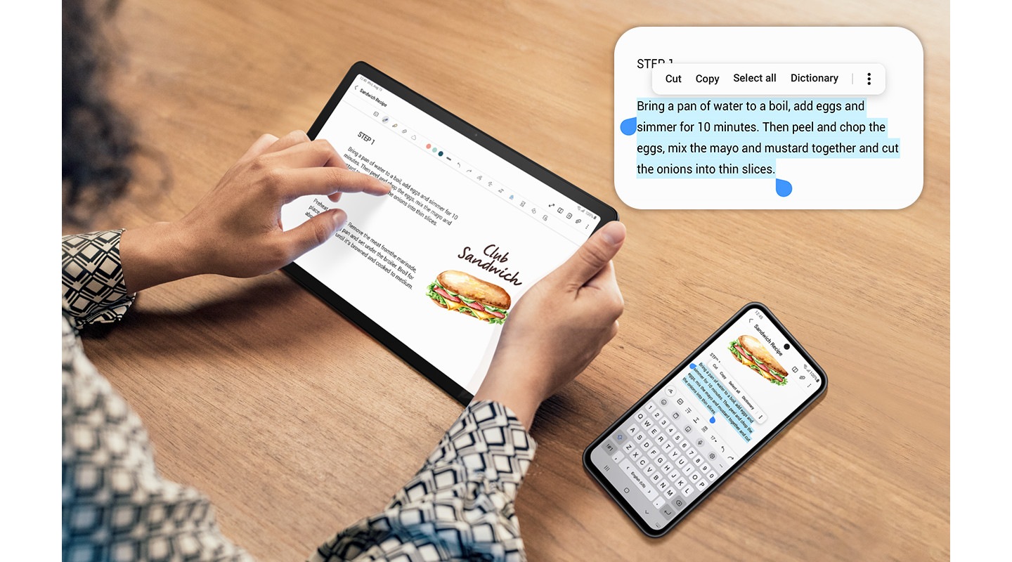 O persoană atinge Galaxy Tab A9+.  În dreapta este un smartphone Galaxy.  Ambele dispozitive afișează același ecran.  Smartphone-ul are o parte din text selectată în albastru, pentru a indica funcția de copiere și inserare pe dispozitive.  Deasupra dispozitivelor este partea selectată mărită, cu opțiuni pentru a selecta toate, tăia, copia, partaja și multe altele.