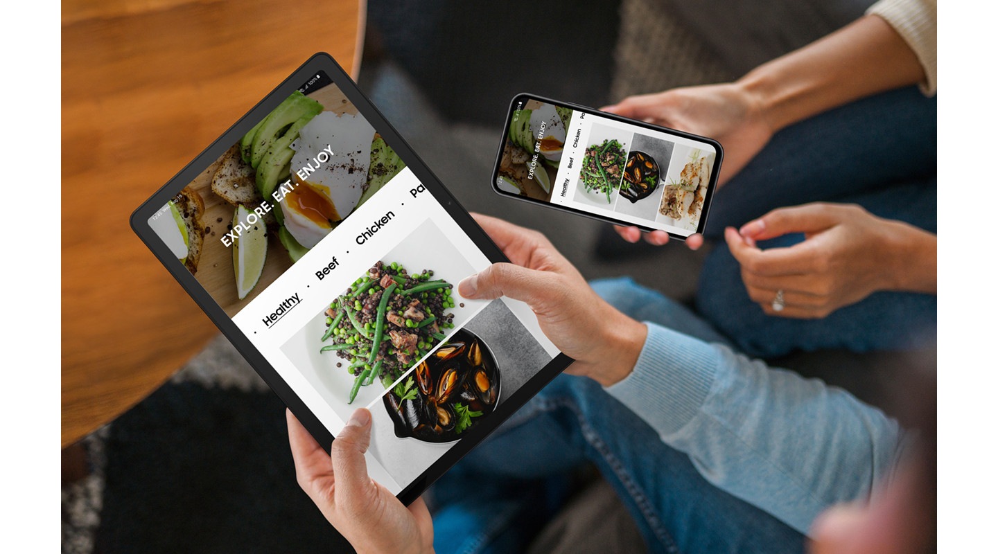 Doi oameni stau unul lângă celălalt.  Persoana din stânga ține în mână un Galaxy Tab A9+, iar persoana din dreapta ține în mână un smartphone Galaxy.  Ambele dispozitive afișează aceeași pagină web legată de alimente.