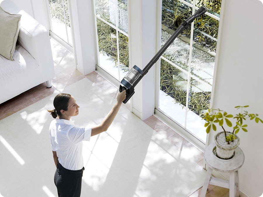 A woman vacuums a high window sill with a Bespoke Jet Plus.
