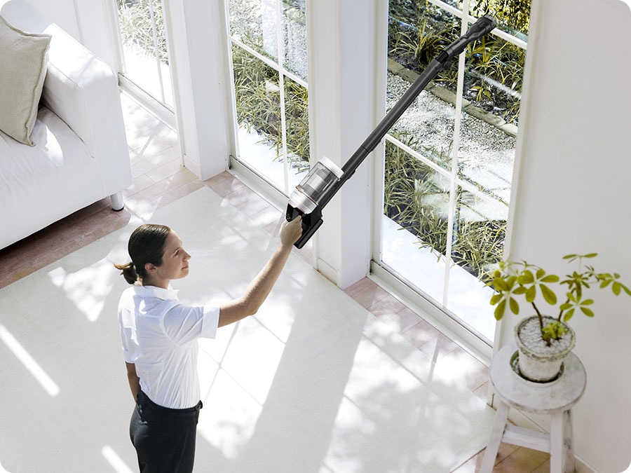 A woman vacuums a high window sill with a Bespoke Jet Plus.