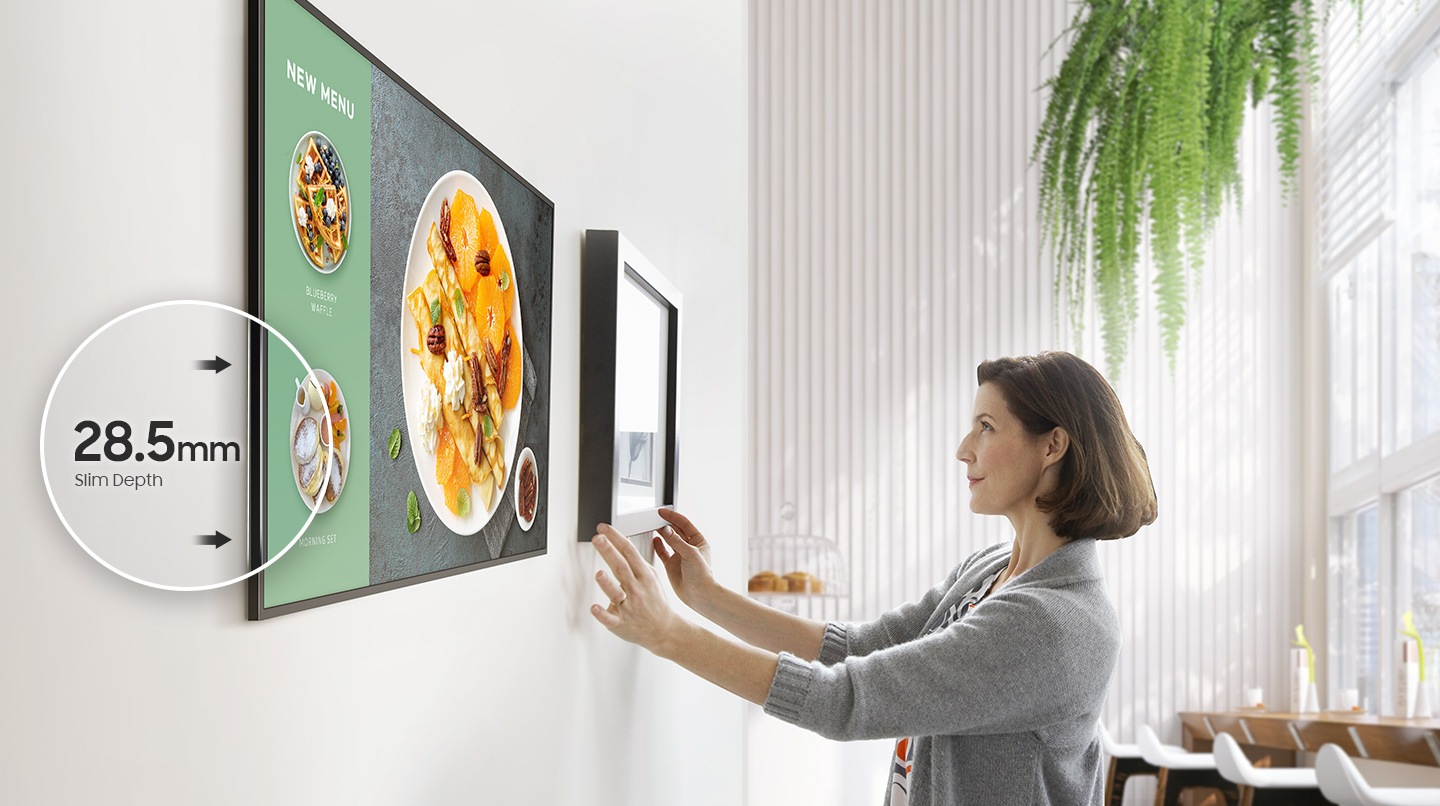 QM32C is installed on the wall of the store. A store clerk hangs a picture frame next to the QM32C. The QM32C is 28.5mm thick, which is thinner than the picture frame the staff is hanging on.