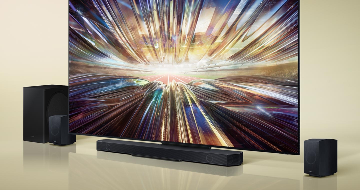 A big-screen TV is surrounded by sound devices, including a Soundbar, a subwoofer and two rear speakers. Roon Tested logo.