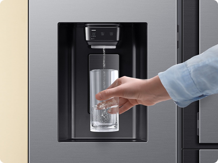 Close-up of a water purifier in the refrigerator. A hand approaches with a cup, filling it with water from the water dispenser.