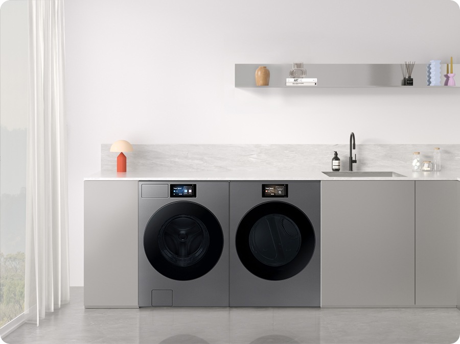 A Bespoke washer and dryer set is installed in various interior spaces: a light gray laundry room, a charcoal-colored kitchen, a white and wood-toned multipurpose space, a dressing room with green cabinets, a laundry room with navy walls, and a modern gray laundry room.