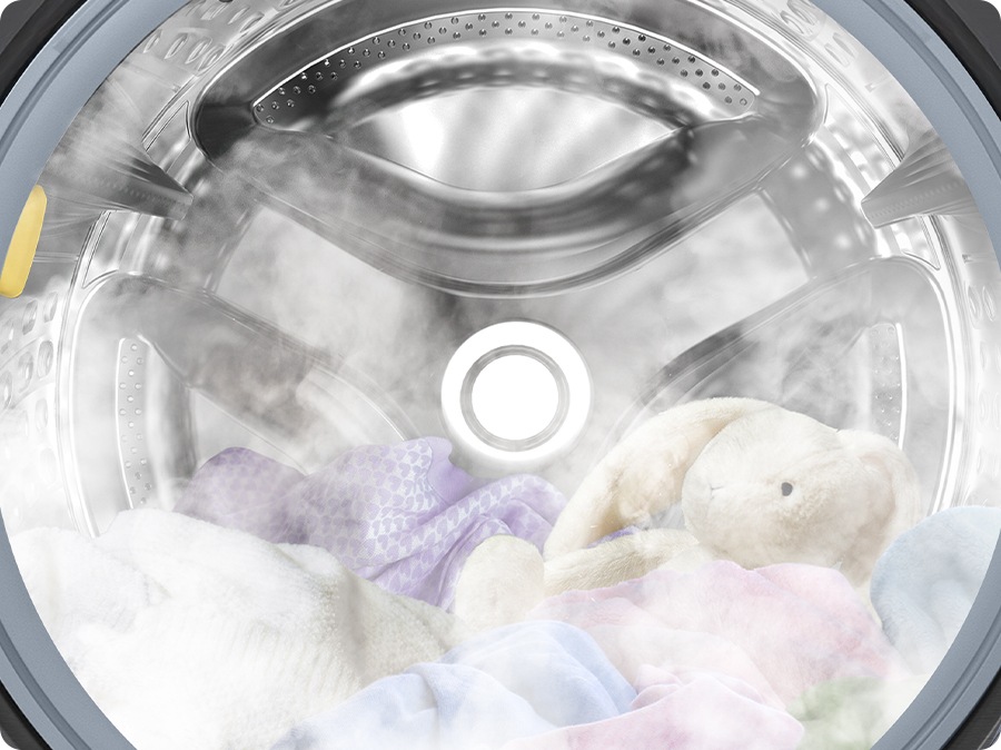 A close-up of towels, clothes, and a bunny doll inside the washer drum, surrounded by steam.