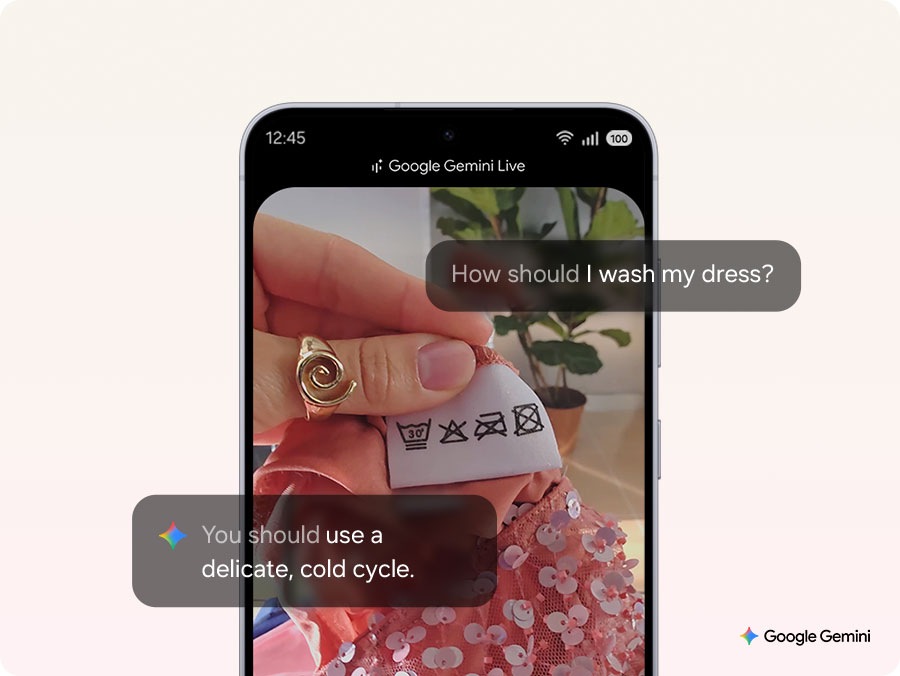A smartphone screen displaying the Google Gemini Live interface. A hand holds a clothing label with washing symbols. The screen shows the question, 'How should I wash my dress?' and the response, 'You should use a delicate, cold cycle.' A sequined dress and a plant are visible in the background.