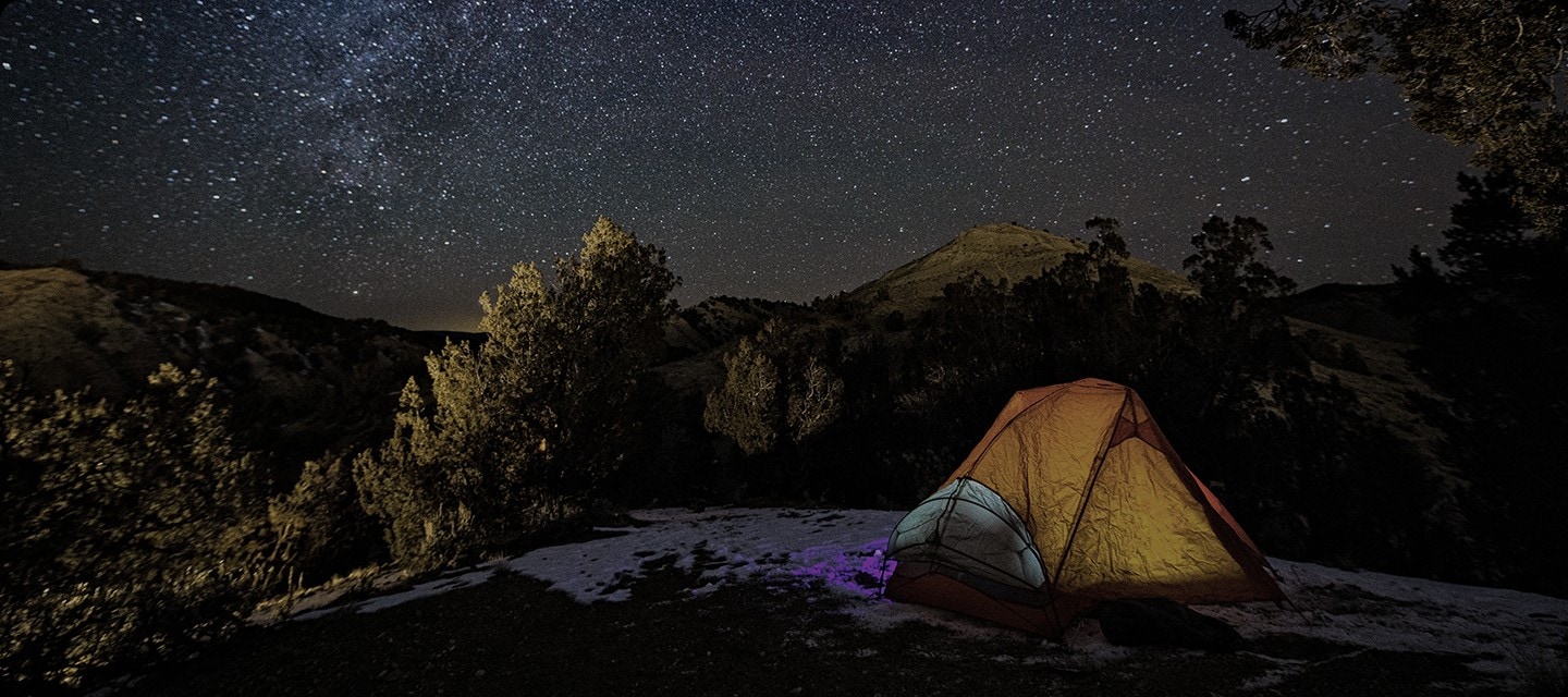 A glowing tent sits on a snowy patch surrounded by trees under a dark, star filled night sky, with a mountain silhouette visible in the background. A square appears at the center of the screen. Inside the square, the image becomes brighter with richer color and deeper contrast and is labeled “OLED HDR Pro,” while the surrounding area remains dimmer and is labeled “SDR.” The square gradually expands to fill the entire screen, transforming the full image into OLED HDR Pro quality as the SDR label disappears and is replaced by “OLED HDR Pro”. HDR 10+ Advanced logo, HDR 10+ Adaptive/Gaming logo.