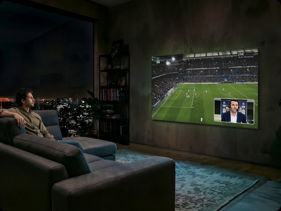 Man watches football on Samsung TV at night. Soundwaves emanate from TV's side and front. He speaks into remote control ‘Bixby, AI Football Mode ON’. AI Football Mode turns on, soundwaves show balanced crowd and commentator sound, and the field looks more crisp and vibrant than when it's off.