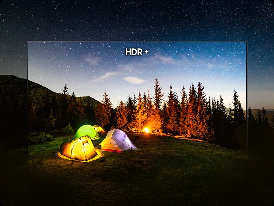 A night camping scene with glowing tents and a bright campfire under a star-filled sky, with a TV screen outline superimposed over the image to illustrate how HDR+ enhances highlights, deepens shadows and reveals richer detail within the display area.