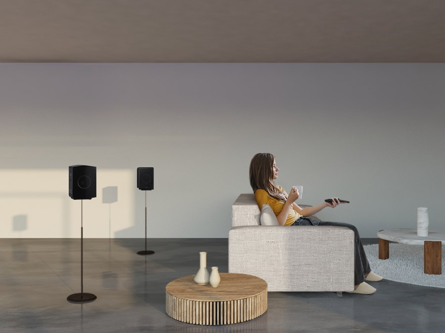 A woman enjoys TV. Soundwave graphics demonstrate Q990B wireless rear speaker's upfiring capability in addition to normal sound output direction when toggle is on.