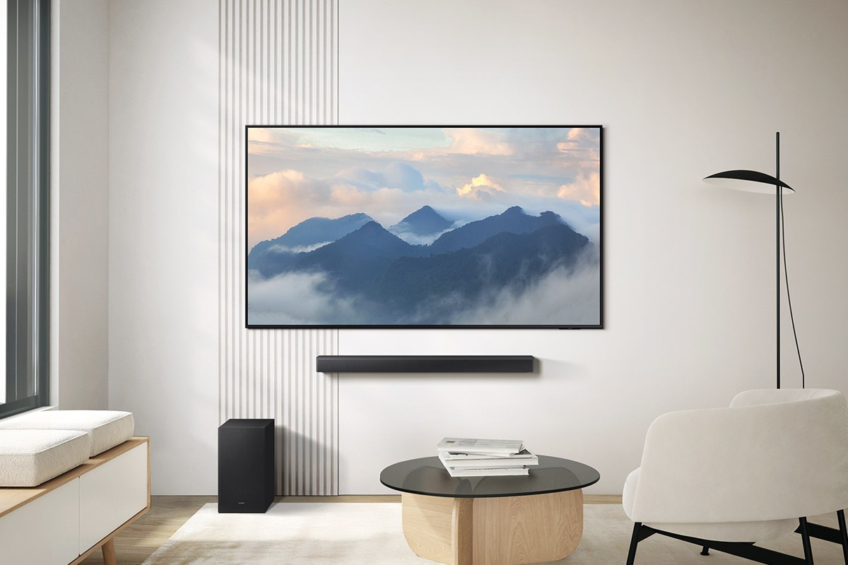 A modern living room showcases a sleek mounted television, playing a tranquil mountain scene with clouds. A round coffee table is placed in front of a comfortable white armchair
