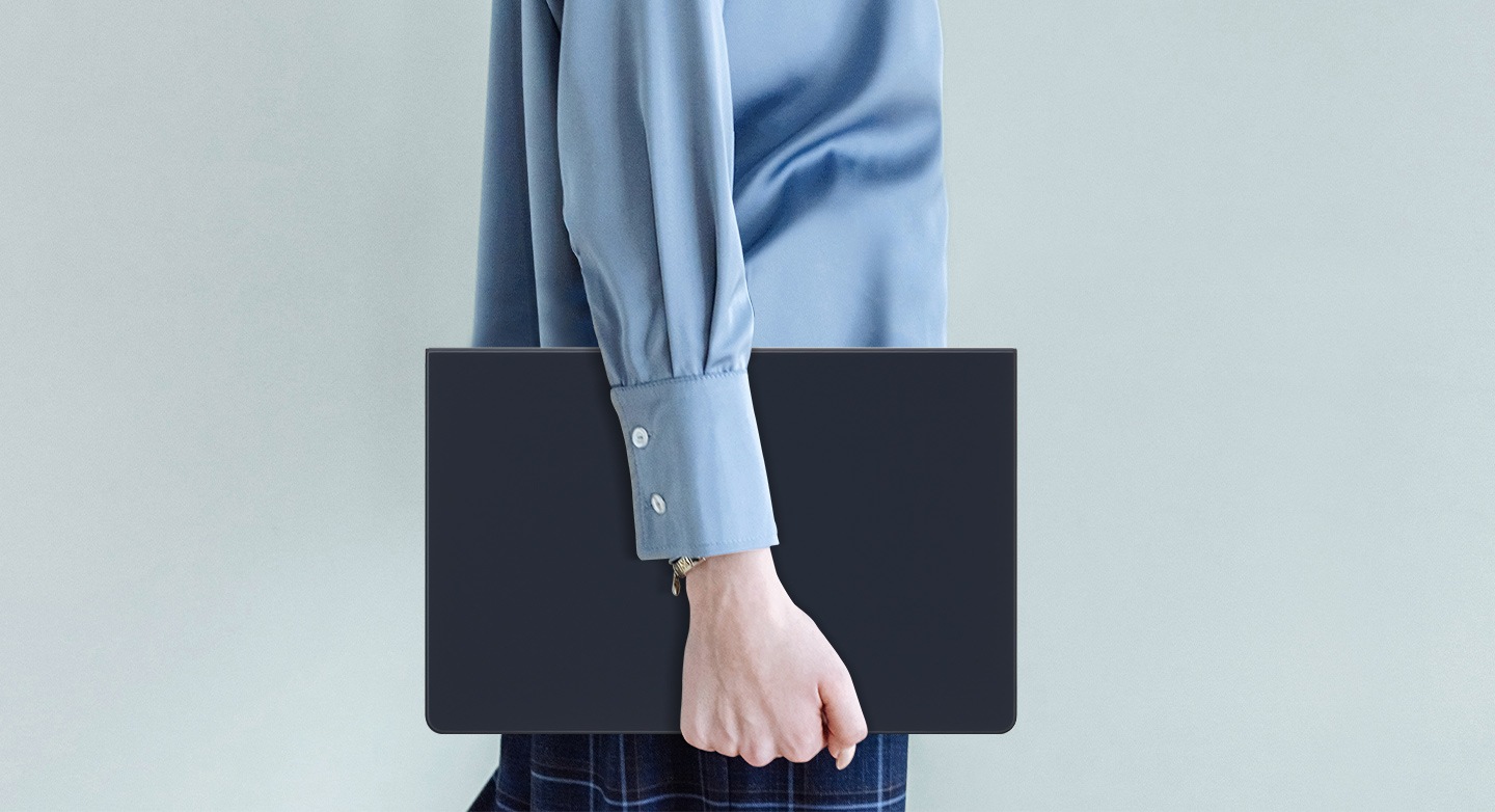 Une personne portant une chemise bleue marche en tenant une Galaxy Tab S9+ équipée d’un Book Cover Keyboard fin.