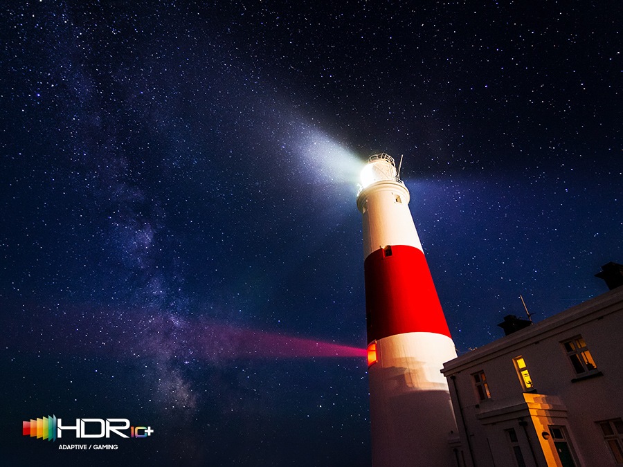 लाइटहाउस से उज्ज्वल प्रकाश एक अंधेरी तारों वाली रात के विपरीत है। HDR10+ अनुकूली/गेमिंग लोगो प्रदर्शन पर है।