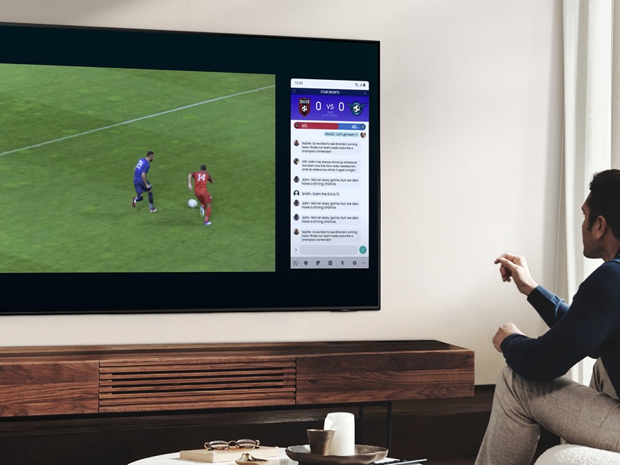 Een man gebruikt de multi -view -functie van Qled om te genieten van een voetbalwedstrijd en tegelijkertijd nieuws op hetzelfde scherm te bekijken