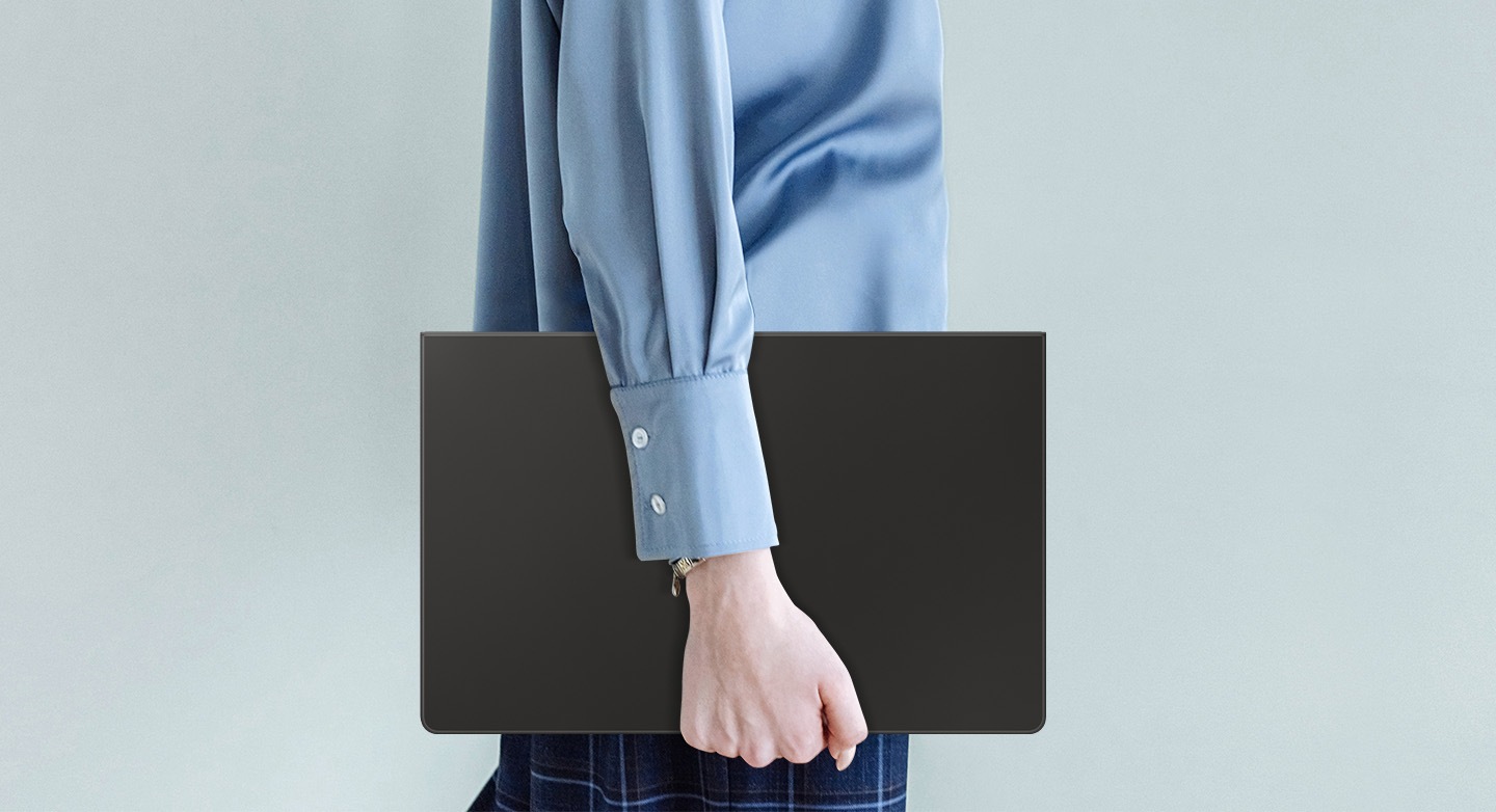 Une personne portant une chemise bleue marche en tenant une Galaxy Tab S10 Ultra équipée d’un Book Cover Keyboard fin.