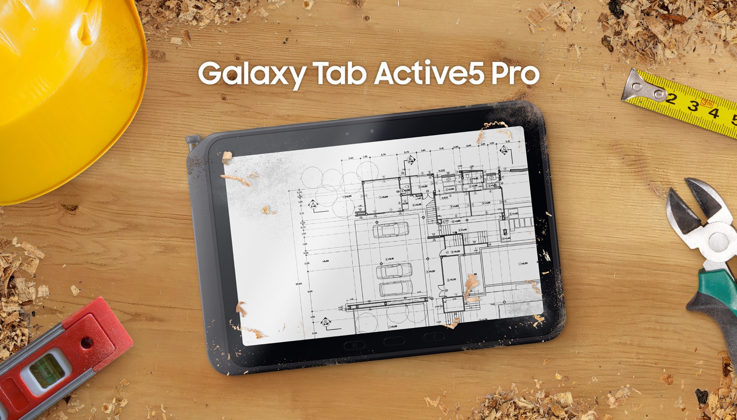 Le Galaxy&nbsp;Tab Active5&nbsp;Pro est placé au centre d’une table affichant un plan. Trouvez rapidement des outils&nbsp;: un casque de sécurité en haut à gauche, un niveau en bas à gauche, un mètre ruban en haut à droite et une clé en bas à droite. Les copeaux de bois sont dispersés sur le bureau, mettant en avant le cadre robuste du lieu de travail.