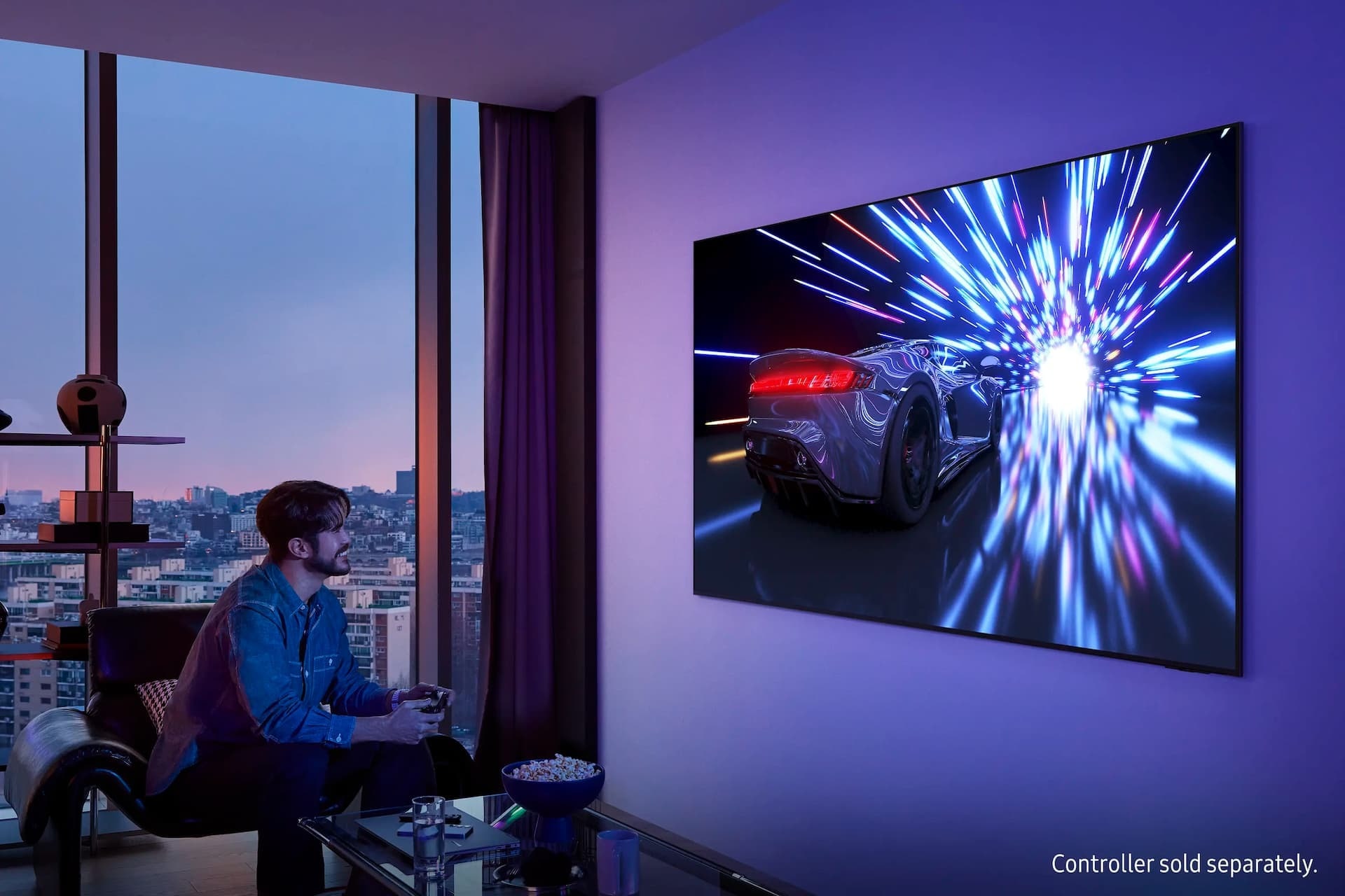 Un homme avec une manette sourit en jouant sur un téléviseur fixé au mur. Le téléviseur affiche une voiture de course qui roule dans un tunnel éclairé.