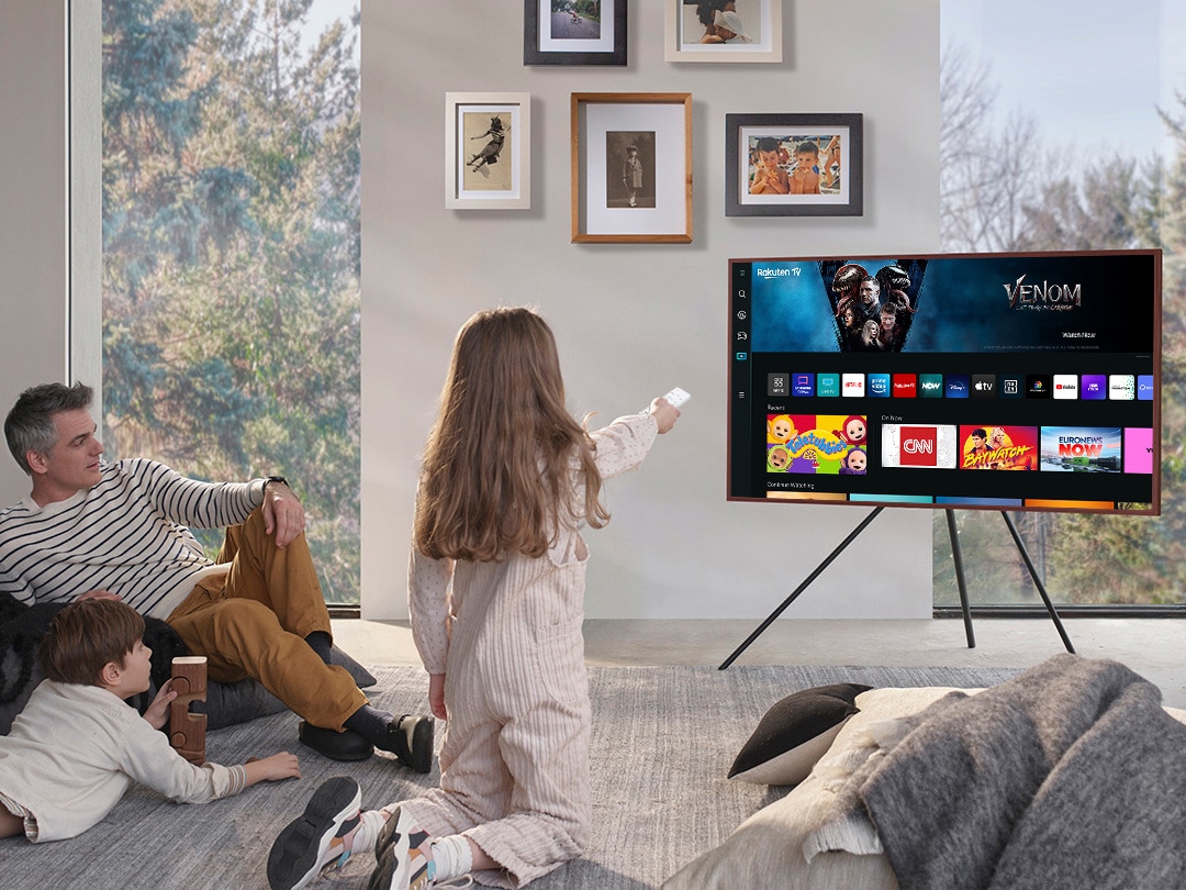 A girl is pointing the remote towards The Frame, which shows the Smart Hub home screen.