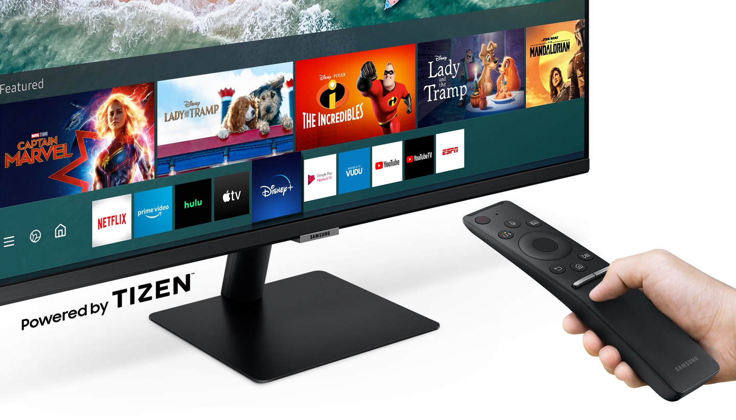 Close up image of an individual holding the Samsung M7 Monitor's remote controller, choosing from a list of entertainment apps such as Disney+, Netflix, YouTube, Hulu, and Amazon Prime displayed on the Smart Hub function.
