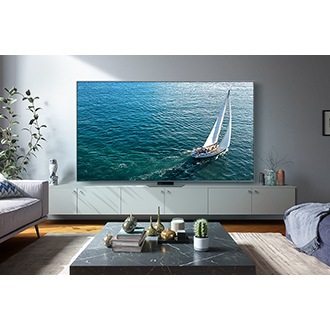 A 98 inch QLED TV is positioned in the living room, showcasing a small boat sailing on the sea on its screen.