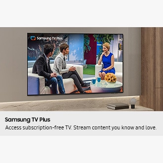 Samsung Mini LED TV mounted on a modern living room wall displaying Samsung TV Plus content, with three people seated in a studio interview setting on screen.