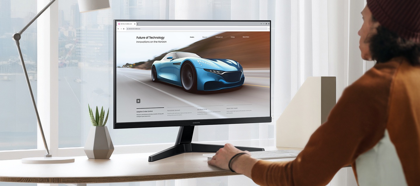 Un escritorio limpio y blanco. Una persona mirando la pantalla del monitor. La pantalla muestra la página de inicio de una empresa automovilística.