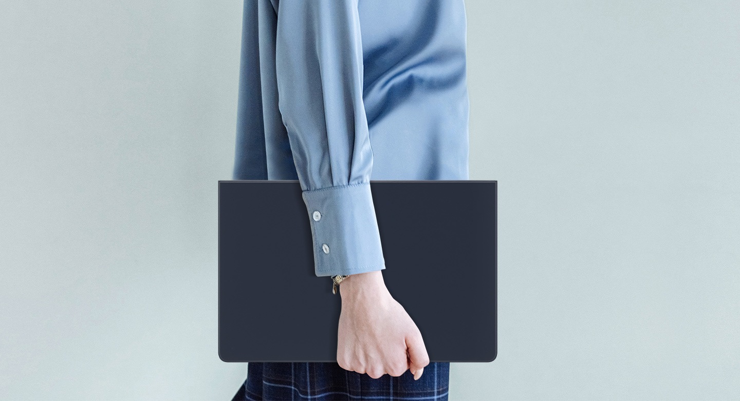 A person in a blue shirt is seen walking while holding a Galaxy Tab S9 covered with Book Cover Keyboard Slim.