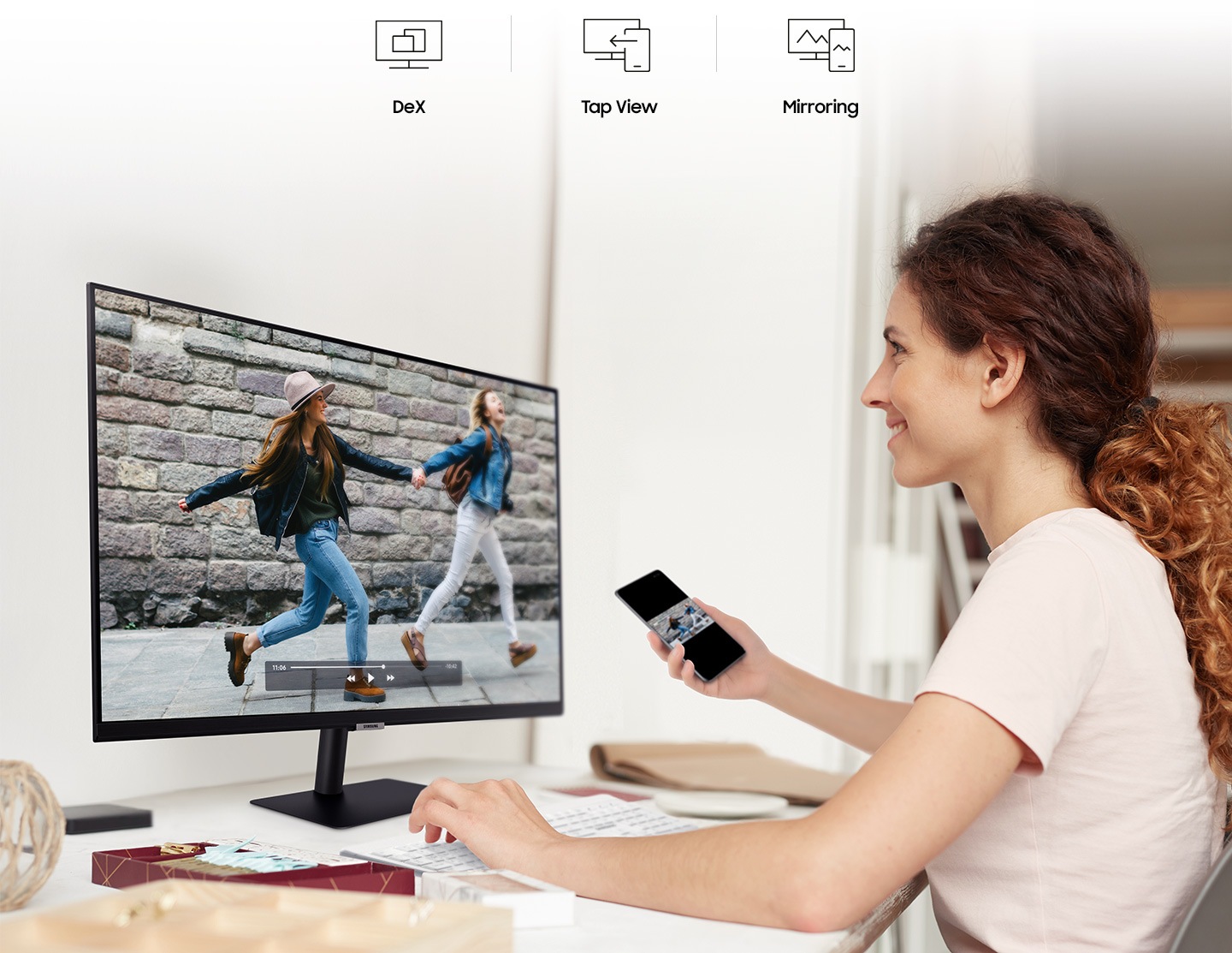 A man connects a smartphone to his monitor using wireless DeX. A smiling woman mirrors videos from her phone to her monitor.