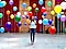 1. There is a close-up shot of a woman standing in the middle of many different color balloons.