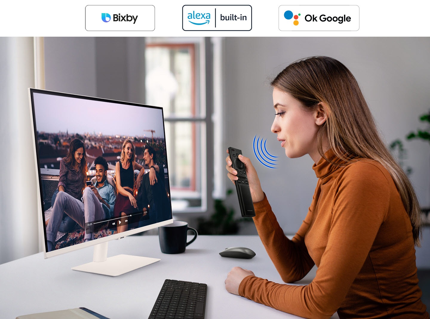 A woman speaks to the monitor. And a video is played on it. The Bixby,  Amazon Alexa and Google Assistant icon is top.