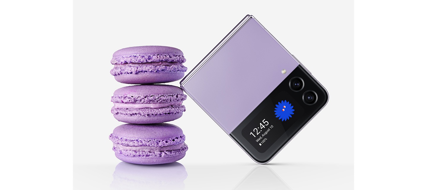 A folded Galaxy Z Flip4 in Bora Purple seen from the Cover Screen. It leans against a stack of three macarons of the same colour. The folded device is similar in size to three stacked macarons.