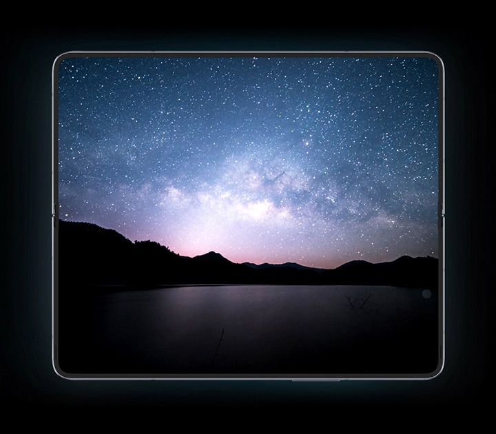 Light passes over the bottom frame of a folded Galaxy Z Fold5 hidden in darkness. Another glimmer reveals the edge of the bottom frame again as the device opens up, revealing the entire device seen from a fully opened Main Screen. A scene of a sport utility vehicle parked on a reflective surface that mirrors a starry night sky is shown on the display.