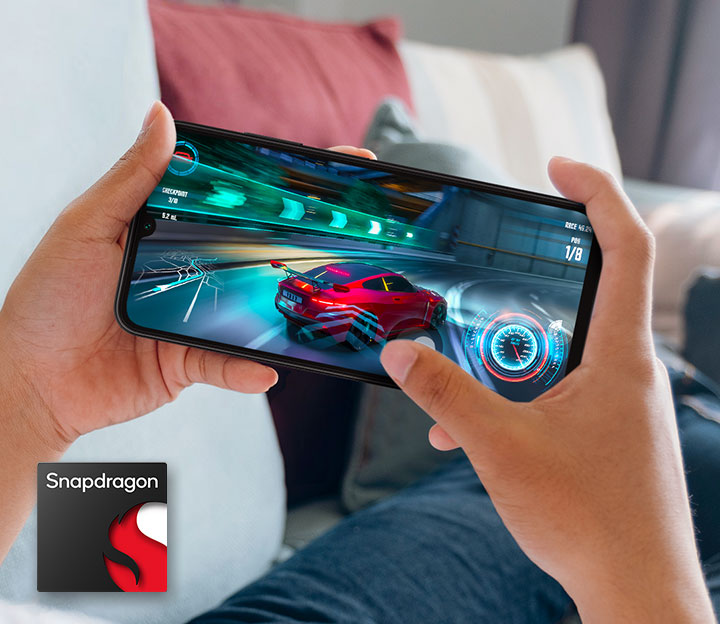 Two hands holding a Samsung Galaxy A05s shows racing gameplay on-screen. At the bottom left corner, the Snapdragon logo is shown.