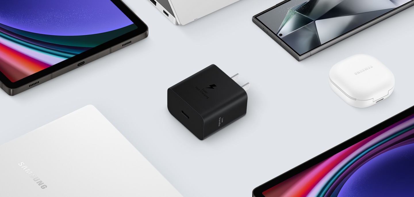 A top view of various Samsung Galaxy devices are shown with a black Power Adapter placed at the center. To the left, a Galaxy Book3, to the right Galaxy Buds2 Pro in White, a Galaxy Tab S9 and Galaxy S24 Ultra are also shown.