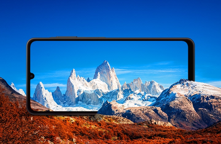 A large Galaxy A06 5G is positioned horizontally between rocky mountains. The screen frames the snowcapped mountains against a blue sky.