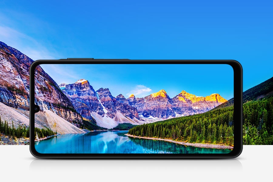 In the background, a river runs between rocky mountains and a forest on a bright day. In the forefront, a Galaxy A06 5G screen positioned horizontally frames the landscape.