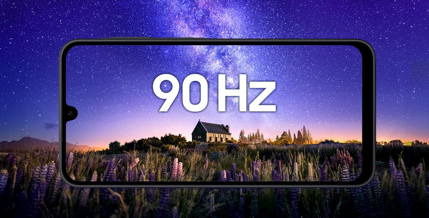 A horizontal view of a black-framed Galaxy A17 smartphone showing a night scene in the background: a stone cottage surrounded by purple flowers under a starry violet-blue sky. '90 Hz' text is centered on the screen, highlighting the display’s smooth motion.