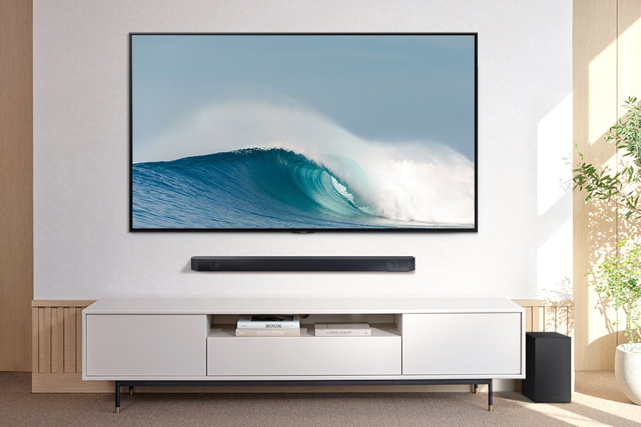 Samsung Soundbar Q600C with Samsung TV mounted on wall above a console with subwoofer on the side.