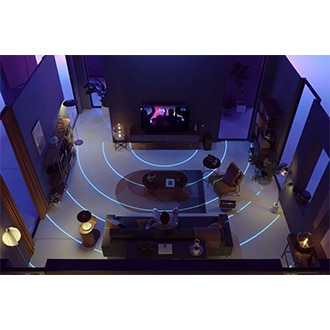 A man is watching TV in a large living room as blue waves illustrate the room being analyzed. SpaceFit Sound Pro optimizes sound to fill the space.